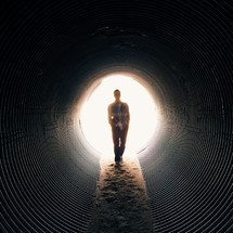 Man walking through dirt in a drainage pipe.