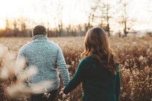 a couple holding hands walking through a field 