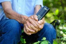 an elderly man clasping a Bible 
