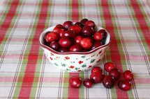 a bowl of cranberries on a plaid table cloth 
