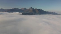 Aerial flight above clouds in mountains in autumn morning landscape
