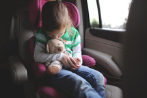 a child in a carseat kissing a teddy bear 