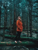 a woman in a coat standing on a fallen tree 