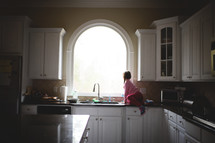 a little girl sitting on a kitchen counter and looking out a window 