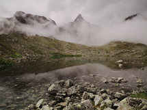 fog and mist in front of mountain peaks nears a stream