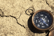 A compass on a parched and cracked ground.
