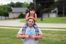 father with daughter on his shoulders standing outdoors