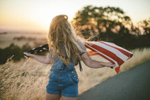 teen girl with an American flag in a field at sunset 