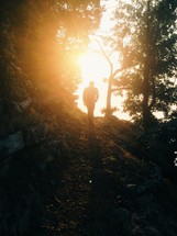 Silhouette of a man walking on a trail through the trees at sunrise.