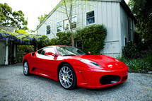 Red ferrari  fast car exotic parked at house in gravel  driveway. 