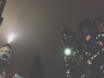 lights shining on skyscrapers at night in a foggy city 