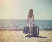 a little girl on a beach holding suitcases 