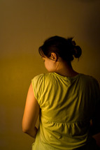 View of woman from behind with partial view of face. Low key image depicting sadness, depression, or loneliness.