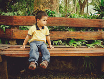 a boy toddler looking worried while sitting on a bench 