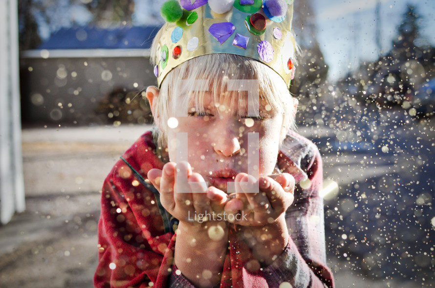 a child dressed as a king blowing glitter 