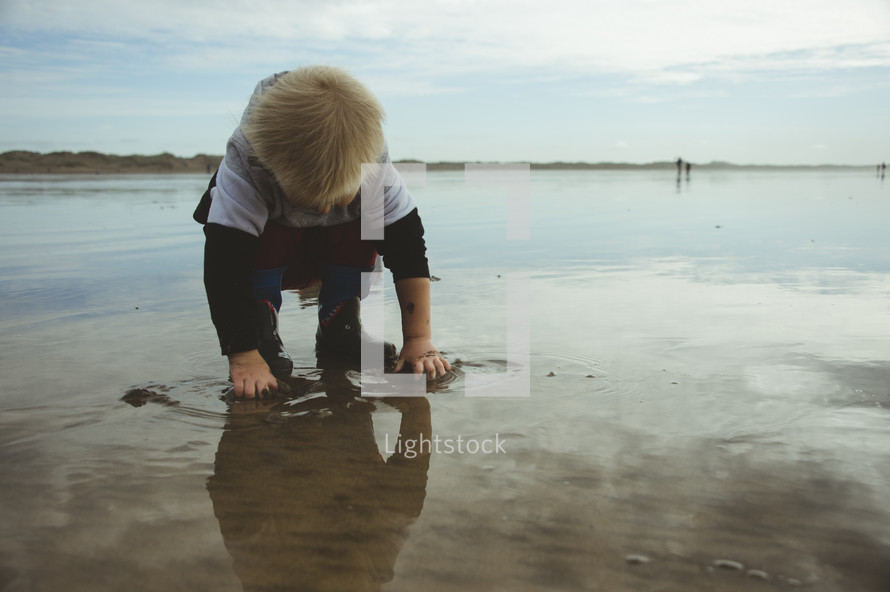a toddler boy playing in wet sand on a beach 