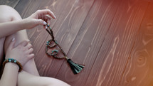 Woman lit hand counts mala beads strands of gemstones used for keeping count during mantra meditations. Lady sits on wooden floor. Spirituality, religion, God concept. Copy space. High quality photo