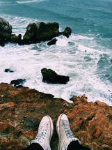 A person's feet on the edge of an oceanside cliff.