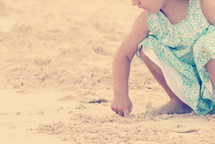a toddler girl playing with sand on a beach 