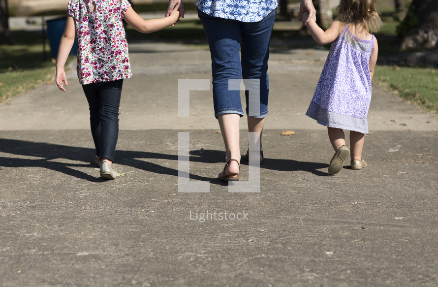 mother and daughters holding hands at a park 