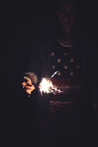 A woman holding a lit sparkler.
