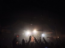 Silhouette of raised hands at a music concert.