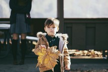 A boy child holding a large fall leaf. 