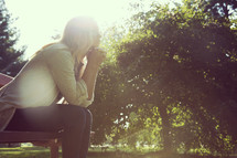 a woman sitting on a park bench with praying hands 