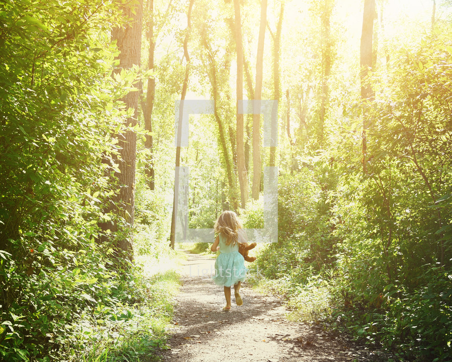 a child with a teddy bear running barefoot on a path through the forest 