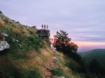 Group standing on a ledge overlooking a valley at sunset.