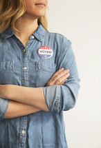 A woman with arms crossed wearing a denim shirt and an ,"I Voted," button.