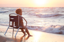 Boy sitting on the chair by sea