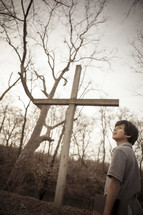 teen boy standing near a cross holding a Bible outdoors 