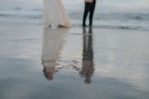 reflection of a bride and groom in wet sand 