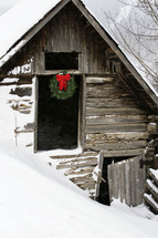 A Christmas wreath hanging on an old barn in the snow. 