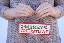 woman in a sweater holding a Merry Christmas sign 