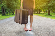 a woman standing on a rural road holding luggage 