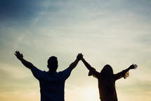 silhouette of a couple standing with raised hands 