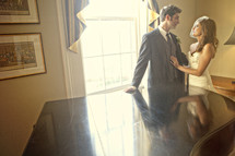 bride and groom standing by grand piano and window
