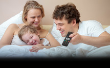 Happy family lying in bed watching television