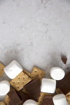 The ingredients for s'mores gathered at the bottom of a marble surface.