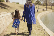 Mother and daughter holding hands while walking in the grass by a lake.