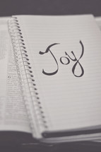 word Joy on a notebook on the pages of a Bible 