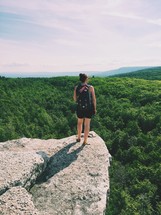 a woman with a backpack standing at the edge of a cliff 