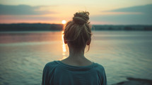 A woman looks toward a sunset facing near water