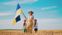 Ukrainian mother with children sons waving national flag in wheat field. Woman in embroidery vyshyvanka. Boys playing flutes. Ukraine, independence, freedom, patriot symbol, VICTORY, win in war.