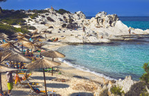 Aegean sea coast with greenery around, rocks and bushes, blue water with waves, Greece