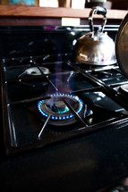 A gas stove top with one burner on, and a copper tea kettle.