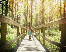 a little girl with a teddy bear running on a wood trail in the woods 
