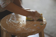 a child scrubbing paint off a stool 